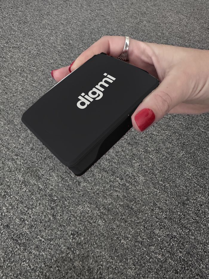 Digmi Box i svart skal med vit Digmi-logga, i en hand