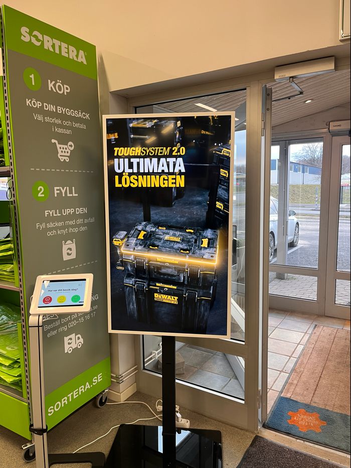 Skärm på golvstativ vid entrén hos Woody Bygghandel